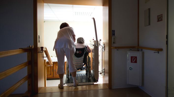 ARCHIV - Eine Pflegerin hilft einer Bewohnerin einer Altenpflegeheimes mit einer Rollstuhlhilfe eine Treppe hinauf, aufgenommen am 26.04.2012 (Quelle: Arno Burgi/dpa).