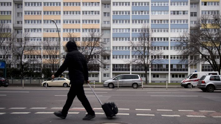 Ein Mann mit einem Rollkoffer geht auf der Frankfurter Allee in Berlin an Plattenbauten vorbei. (Quelle: imago/IPON)