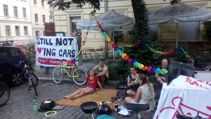 "Still not Loving Cars" steht auf einem Schild geschrieben. Teilnehmer des "Park(ing) Days" in Berlin picknicken (Verein "autofrei leben!")