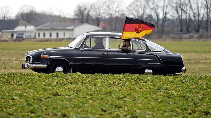 Symbolbild: Zwei Männer fahren mit einem Tatra 603 und wehender DDR Flagge übers Land. (Quelle: imago images/Jens Koehler)