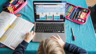 Auf einem Wohnzimmertisch steht ein Laptop an dem gerade ein Kind arbeitet, daneben liegen verschiedene Schulutensilien und ein aufgeschlagenes Buch. (Quelle: dpa/K. Schmitt)