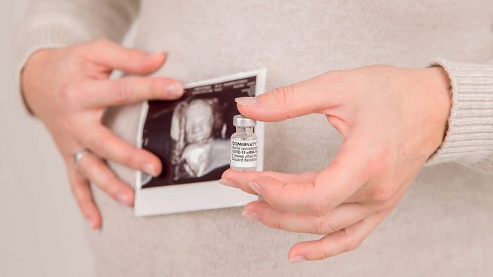 Symbolbild: Eine schwangere Frau hält eine Impfdose vor ihrem Babybauch. (Quelle: imago images/K. Schmitt)