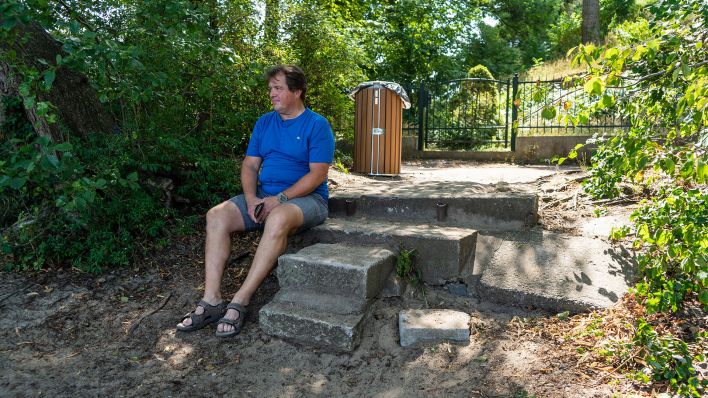 Der Strausberger Anwalt Jens Mader sitzt auf einer Steintreppe und schaut auf den See, 20.07.2022 (Quelle: rbb /Hinze).