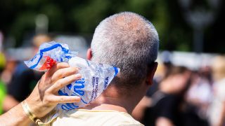 Symbolbild: Eine Person hält einer anderen bei der Technoparade "Rave the Planet" im Juli 2023 auf der Straße des 17. Juni einen Eisbeutel in den Nacken. (Quelle: dpa/Christoph Soeder)