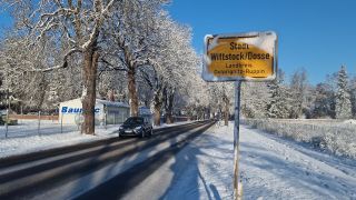Das Ortseingangsschild von Wittstock/Dosse steht am verschneiten Straßenrand. (Quelle: dpa/Cevin Dettlaff)