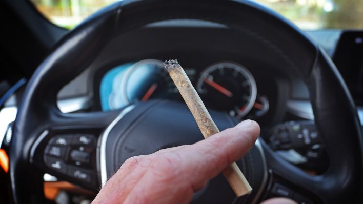 Symbolbild:Ein Mann sitzt mit einem Joint zwischen den Fingern am Steuer eines Autos.(Quelle:dpa/K.-J.Hildenbrand)