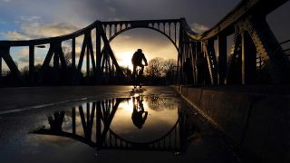 Ein Radfahrer fährt bei Sonnenuntergang auf der Glienicker Brücke zwischen Berlin und Potsdam: (Foto: IMAGO / Martin Müller)