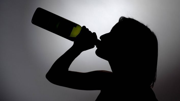 SYMBOLBILD: Silhouette einer jungen Frau, die aus einer Weinflasche trinkt