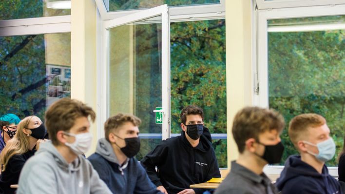 19.10.2020, Hamburg: Schüler einer 13. Klasse der Oberstufe der Stadtteilschule Niendorf sitzen mit Mund-Nasen-Bedeckungen im Deutsch-Unterricht vor einem geöffneten Fenster.