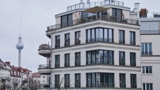 Hinter einem Neubau und einer Häuserreihe mit Altbauten im Stadtteil Prenzlauer Berg ragt der Berliner Fernsehturm in die Höhe.