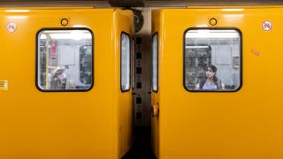 Zwei Personen mit Mund-Nasen-Maske sitzen in unterschiedlichen Waggons der U-Bahn in Berlin (Bild: picture alliance / photothek | Florian Gaertner)