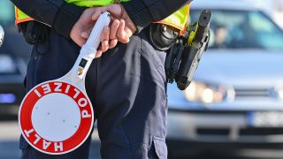 Ein Beamter der Bundespolizei steht am deutsch-polnischen Grenzübergang mit einer Kelle mit der Aufschrift "Halt Polizei".