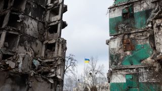 Kyiv: Ukraine Flagge im Hintergrund zwischen zwei zerstörten Häusern © picture alliance / AA | Oleksii Chumachenko