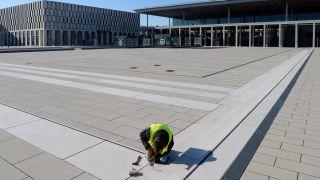Ein Handwerker arbeitet am 24.02.2014 an den Bodenplatten vor der Kulisse des neuen Hauptstadtflughafens in Schönefeld (Brandenburg) (Quelle: dpa)