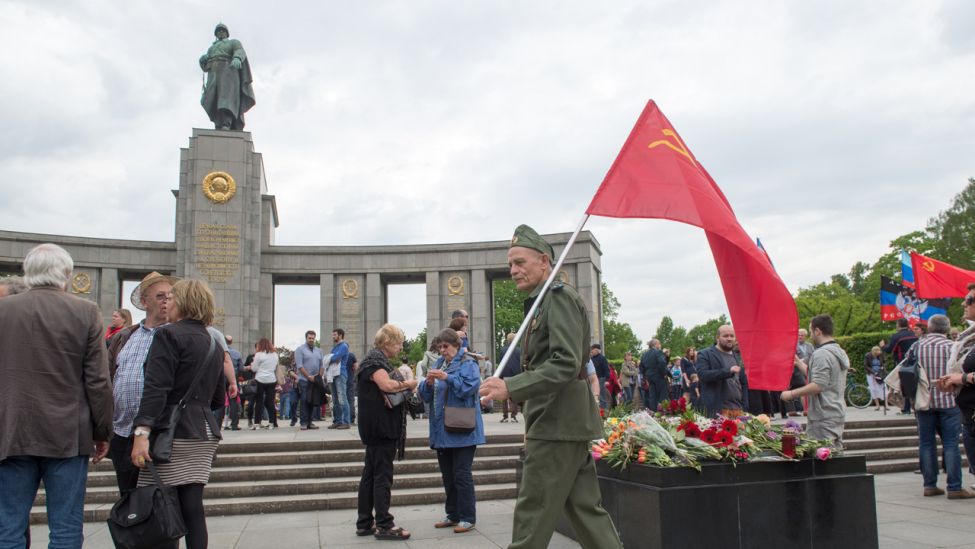 Ein Mann in historischer Uniform läuft mit einer sowjetischen Fahne am 09.05.2015 in Berlin vor dem Sowjetische Ehrenmal an der Straße des 17. Juni vorbei. (Quelle: dpa)