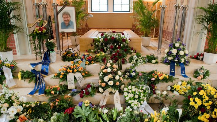 Blumensträuße und Gestecke liegen am 15.01.2016 in Cottbus (Brandenburg) in der Kapelle auf dem Südfriedhof nach der Trauerfeier für den am 04.01.2016 verstorbenen Entertainer Achim Mentzel vor dessen Porträtbild. (Quelle: dpa)