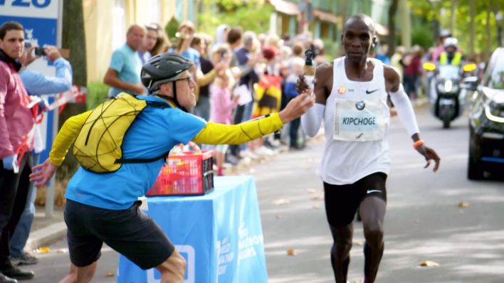 "Claus-Henning Schulke reicht Marathonläufer Eliud Kipchoge eine Wasserflasche beim Berlin-Marathon 2018"; © rbb