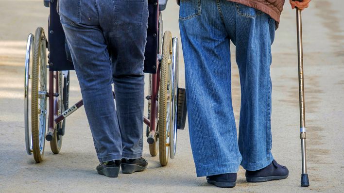 Mann und Frau gehen mit Rollstuhl und Gehstock spazieren; Quelle: McPHOTO/E.Wodicka/imago/blickwinkel
