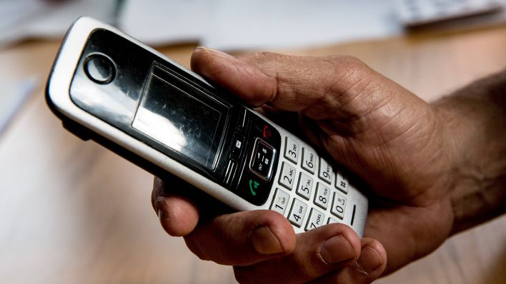 Hand hält älteres Modell eines schnurlosen Telefons (Bild: imago/Fotostand)