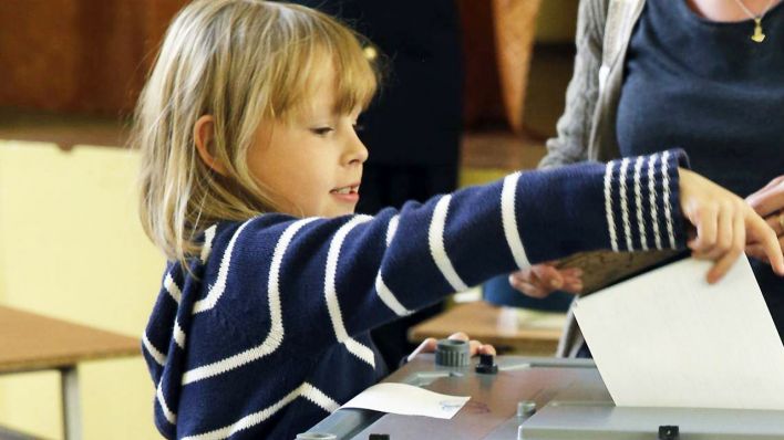 Kind steckt Wahlunterlagen in Wahlurne (Quelle Archivbild: imago/Russian Look)
