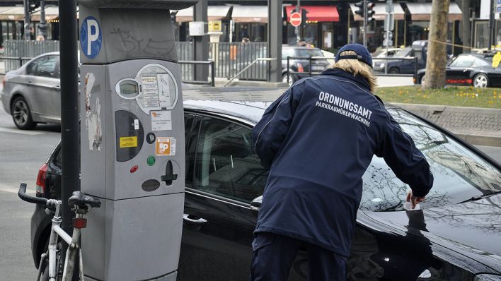 Eine Mitarbeiterin des Berliner Ordnungsamts klemmt ein "Knöllchen" hinter den Scheibenwischer eines Autos (Quelle: imago / Steinach)
