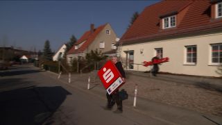 Ein Mittarbeiter trägt ein demontiertes Schild der mittelbrandenburgischen Sparkasse zu einem Transporter (Quelle: rbb Fernsehen/ Abendschau)