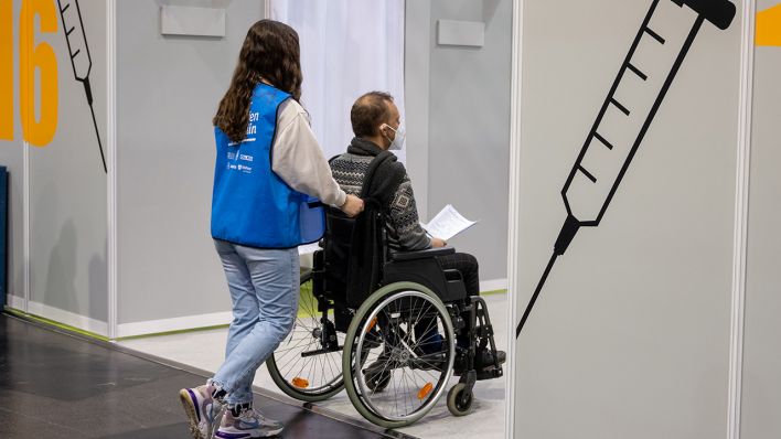 Archivbild: Im Impfzentrum im Velodrom schiebt eine Helferin bei einem Probelauf einen Statisten im Rollstuhl durch einen Gang. (Quelle: dpa/C. Gateau)