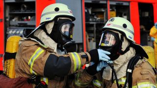 Ein Feuerwehrmann überprüft Atemschutz-Gerät seines Kollegen. (Quelle: dpa/Paul Zinken)
