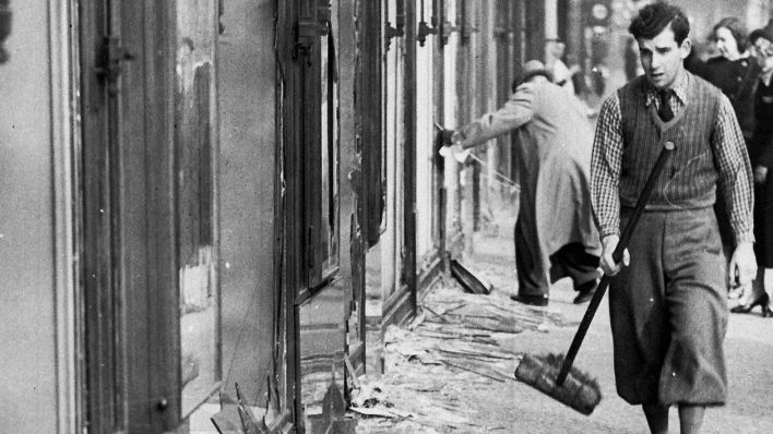 Ein historisches Foto vom 10.11.1938 zeigt einen Mann, der am Tag nach der "Reichskristallnacht", dabei ist die Scherben eines zerbrochenen Fensters eines jüdischen Geschäfts in Berlin aufzukehren. (Bild: dpa)