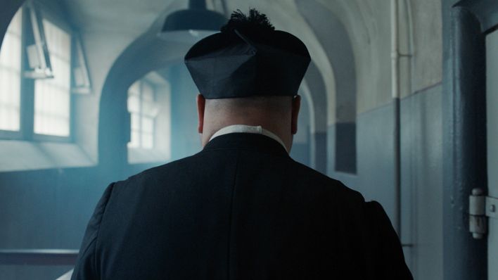 Standbild aus Babylon Berlin: Pater Wilczek (Frank Küster) auf dem Weg durch einen histotrischen Zellentrack zu einem Gefangenen. (Bild: X Filme | ARD Degeto | sky | Beta)