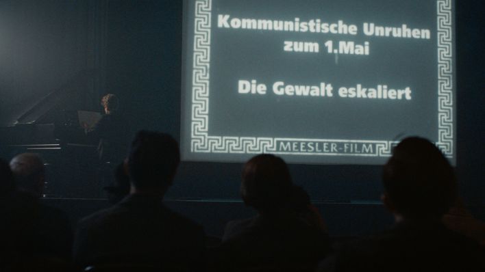 Standbild aus Babylon Berlin: Das Publikum verfolgt gespannt die Wochenschau, die in einem kleinen Kinosaal vorgeführt wird. (Quelle: X Filme | ARD Degeto | sky | Beta)
