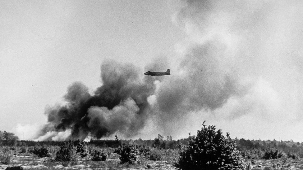 Start eines US-Militärflugzeuges vom Flughafen Frankfurt am Main; im Hintergrund steigt Rauch von einer abgestürzten und in Brand geratenen Maschine auf.