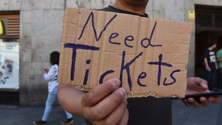 Ein Mann hält ein bemaltes Pappschild "Need Tickets" (Quelle:imago/Milner)