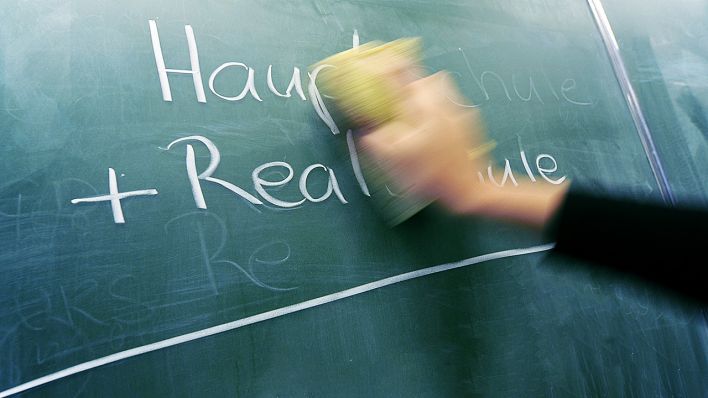 Illustration - Eine junge Frau wisch am Donnerstag mit einem Schwamm die Worte "Hauptschule + Realschule auf einer Tafel in einer Schule weg. (Quelle: dpa/Steffen)