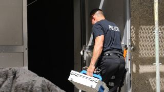 Ein Polizist geht mit einem Koffer in ein Wohngebäude in der Innenstadt.