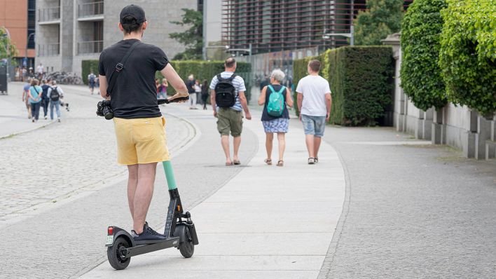 Ein Mann auf dem E-Scooter im Regierungsviertel fährt auf dem Gehweg mit Fußgängern. (Quelle: imago images/Chris Emil Janssen)