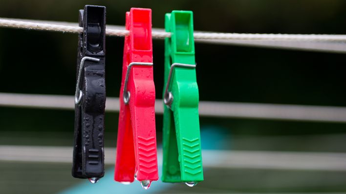 Symbolbild - Wäscheklammern in schwarz, rot und grün hängen an einer Wäscheleine (Bild: dpa/Patrick Pleul)