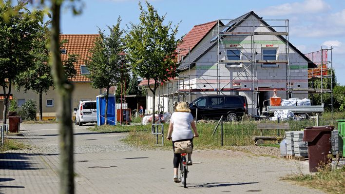 Eine Frau fährt mit dem Fahrrad am Stadtrand, im Speckgürtel der Großstadt auf ein Einfamilienhaus zu. (Quelle: dpa/Woitas)