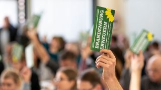 Grünen-Delegierter hält beim Kleinen Parteitag in Brandenburg eine Stimmkarte in die Höhe (Bild: dpa/Fabian Sommer)