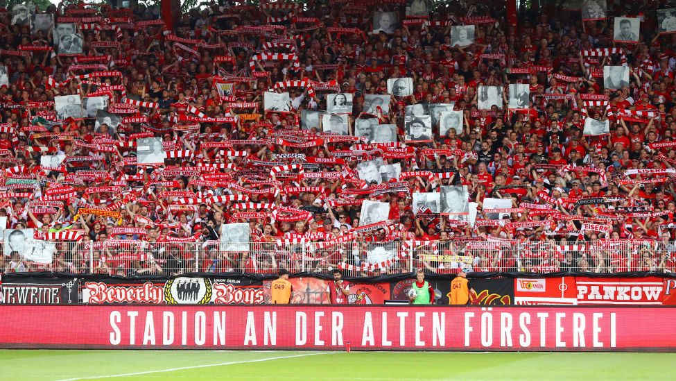 Fans des 1. FC Union Berlin halten auf der Tribüne Fotos verstorbener Fans hoch. Bild: Imago/Picture Point LE.