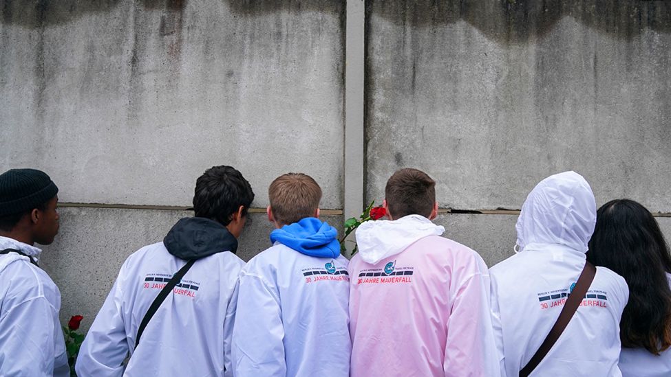 09.11.2019, Berlin: Jugendliche aus Norwegen blicken bei der Gedenkveranstaltung der Stiftung Berliner Mauer an der Bernauer Straße durch einen Mauerspalt. (Quelle: dpa/Nietfeld)