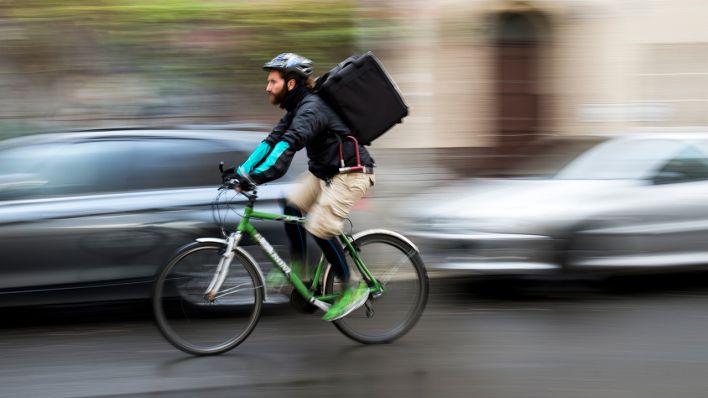Symbolbild: Ein Fahrradkurier fährt mit seinem Fahrrad und einer Lieferung auf dem Rücken durch den Stadtverkehr in Berlin. (Quelle: dpa/Gregor Fischer)