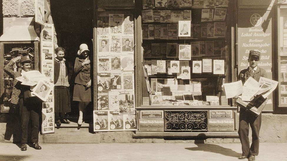 Zeitschriftengeschäft in Berlin um 1925, mit zwei Zeitungskolporteuren mit Kappen im Vordergrund. (Quelle: Austrian Archives)