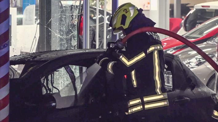 Ein Feuerwehrmann löscht ein ausgebranntes Auto vor dem Potsdamer Autohaus (Bild: rbb)