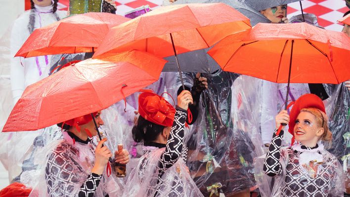 23.02.2020, Brandenburg, Cottbus: Tanzmariechen des "Karneval Verband Lausitz 1990" suchen auf einer Tribüne beim "Zug der fröhlichen Leute" unter Regenschirmen Schutz (Quelle: dpa/Oliver Killig)