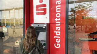 Eine junge Frau steht vor einem Geldautomat der Sparkasse. (Quelle: imago-images/Sven Simon)