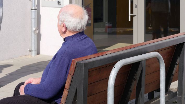 Ein älterer Mann sitzt auf einer Bank vor einem Gebäude. (Quelle: imago-images/Sabine Gudath)