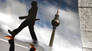 Fußgänger und Fernsehturm spiegeln sich in Pfütze (Quelle: dpa/Simon Frohn)