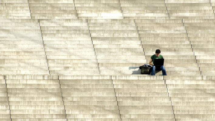 Mann sitzt alleine auf Treppenstufen und arbeitet an Laptop (Quelle: dpa/Michael Dietrich)