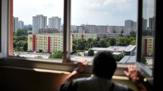 Ein Mann blickt in Berlin aus einem Fenster im elften Stock eines Hochhauses über Wohnblocks im Stadtteil Marzahn. (Quelle: dpa/Britta Pedersen)